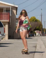 Busty skateboard chick Dharma Webb in tight shorts rides to the beach to swim in sexy bikini and to get a tan