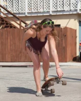 Busty skateboard chick Dharma Webb in tight shorts rides to the beach to swim in sexy bikini and to get a tan