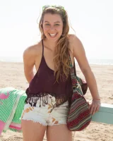 Busty skateboard chick Dharma Webb in tight shorts rides to the beach to swim in sexy bikini and to get a tan