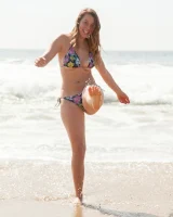 Busty skateboard chick Dharma Webb in tight shorts rides to the beach to swim in sexy bikini and to get a tan