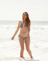 Busty skateboard chick Dharma Webb in tight shorts rides to the beach to swim in sexy bikini and to get a tan