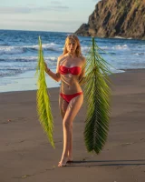 Blonde beach fairy in red bikini with green palm leaf strips her puffy nipples sexy body