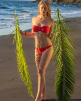 Blonde beach fairy in red bikini with green palm leaf strips her puffy nipples sexy body