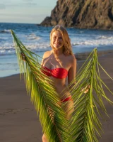 Blonde beach fairy in red bikini with green palm leaf strips her puffy nipples sexy body