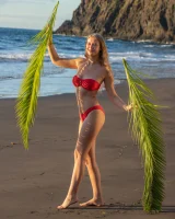 Blonde beach fairy in red bikini with green palm leaf strips her puffy nipples sexy body