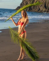 Blonde beach fairy in red bikini with green palm leaf strips her puffy nipples sexy body