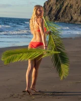Blonde beach fairy in red bikini with green palm leaf strips her puffy nipples sexy body