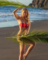 Blonde beach fairy in red bikini with green palm leaf strips her puffy nipples sexy body