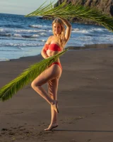 Blonde beach fairy in red bikini with green palm leaf strips her puffy nipples sexy body