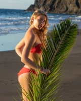 Blonde beach fairy in red bikini with green palm leaf strips her puffy nipples sexy body