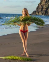 Blonde beach fairy in red bikini with green palm leaf strips her puffy nipples sexy body
