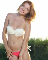 Exciting redhead in white and red bikini is playing nude on the beach by the lake