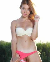 Exciting redhead in white and red bikini is playing nude on the beach by the lake