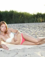 Exciting redhead in white and red bikini is playing nude on the beach by the lake