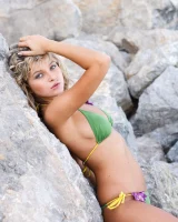 Beautiful blonde in green bikini strips at the rocks seaside