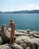 Exciting blonde in red micro bikini is nude on the sea rocks