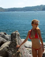 Exciting blonde in red micro bikini is nude on the sea rocks