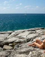 Exciting blonde in red micro bikini is nude on the sea rocks