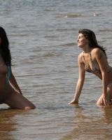 Two girlfriends in bikinis poses in the water outside