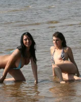 Two girlfriends in bikinis poses in the water outside
