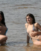 Two girlfriends in bikinis poses in the water outside