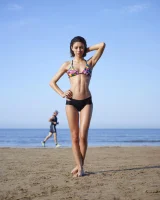 Wonderful chick with tight body is on the beach in sexy bikini and nude on the sand aside at the rocks