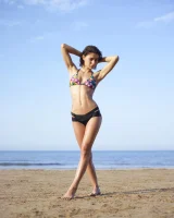 Wonderful chick with tight body is on the beach in sexy bikini and nude on the sand aside at the rocks