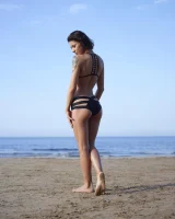 Wonderful chick with tight body is on the beach in sexy bikini and nude on the sand aside at the rocks