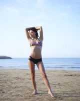 Wonderful chick with tight body is on the beach in sexy bikini and nude on the sand aside at the rocks