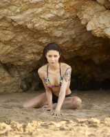 Wonderful chick with tight body is on the beach in sexy bikini and nude on the sand aside at the rocks