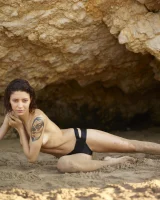 Wonderful chick with tight body is on the beach in sexy bikini and nude on the sand aside at the rocks