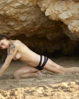 Wonderful chick with tight body is on the beach in sexy bikini and nude on the sand aside at the rocks