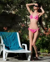 Young slim body brunette beauty is by the pool in polka dot pink bikini with sunglasses