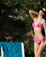 Young slim body brunette beauty is by the pool in polka dot pink bikini with sunglasses