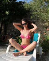 Young slim body brunette beauty is by the pool in polka dot pink bikini with sunglasses