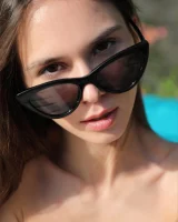 Young slim body brunette beauty is by the pool in polka dot pink bikini with sunglasses