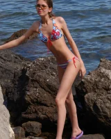 Hot young baby in motley bikini undresses on the rocky sea shore to have fun nude with hairy pussy by the water